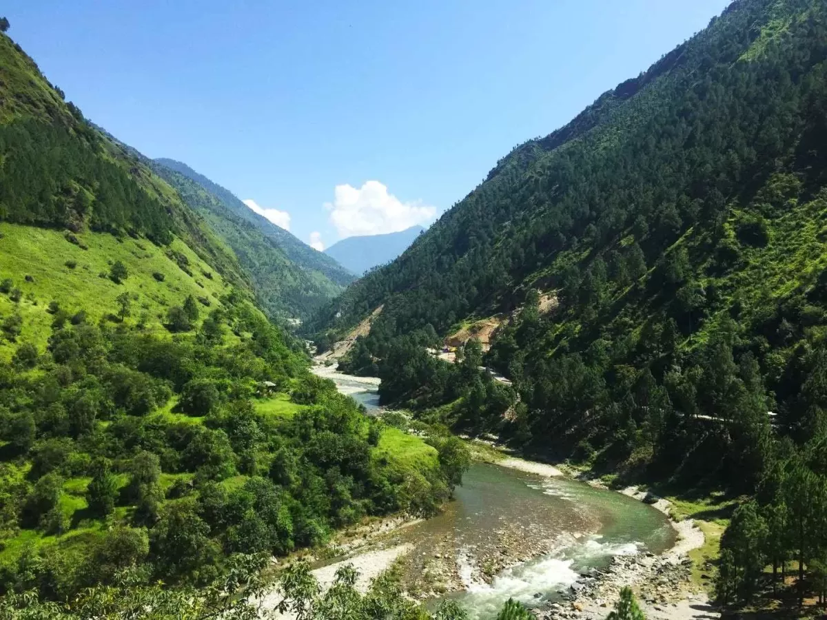 Kufri Himachal Pradesh lush green valley river snaking pine clad mountains blue skies distant peaks road bridge, perfect Himachal Pradesh tour packages.