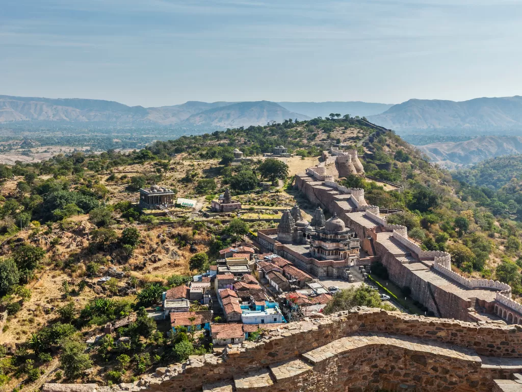 Kumbhalgarh Fort during partly cloudy day, featuring long ramparts, dome shrines, shikhara temples, Aravalli hills, villages, perfect adventure experience Rajasthan tour packages.