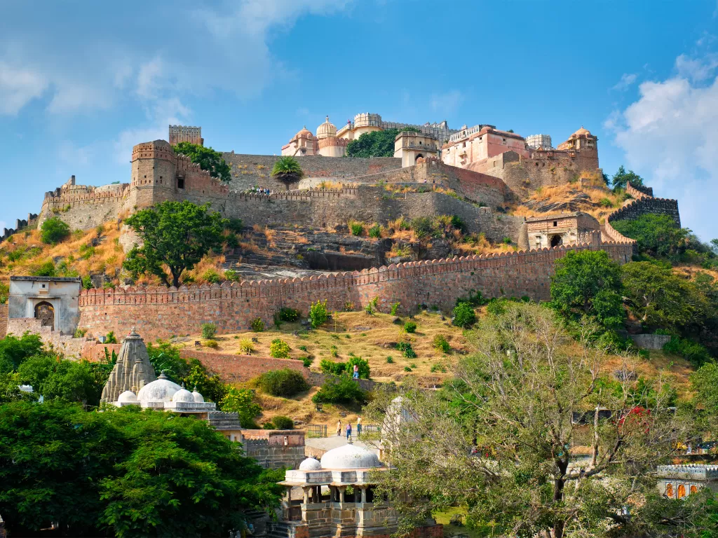 Kumbhalgarh Fort during partly cloudy weather, featuring layered walls, Jain domes, temples, trees, hills, perfect adventure experience Rajasthan tour packages.