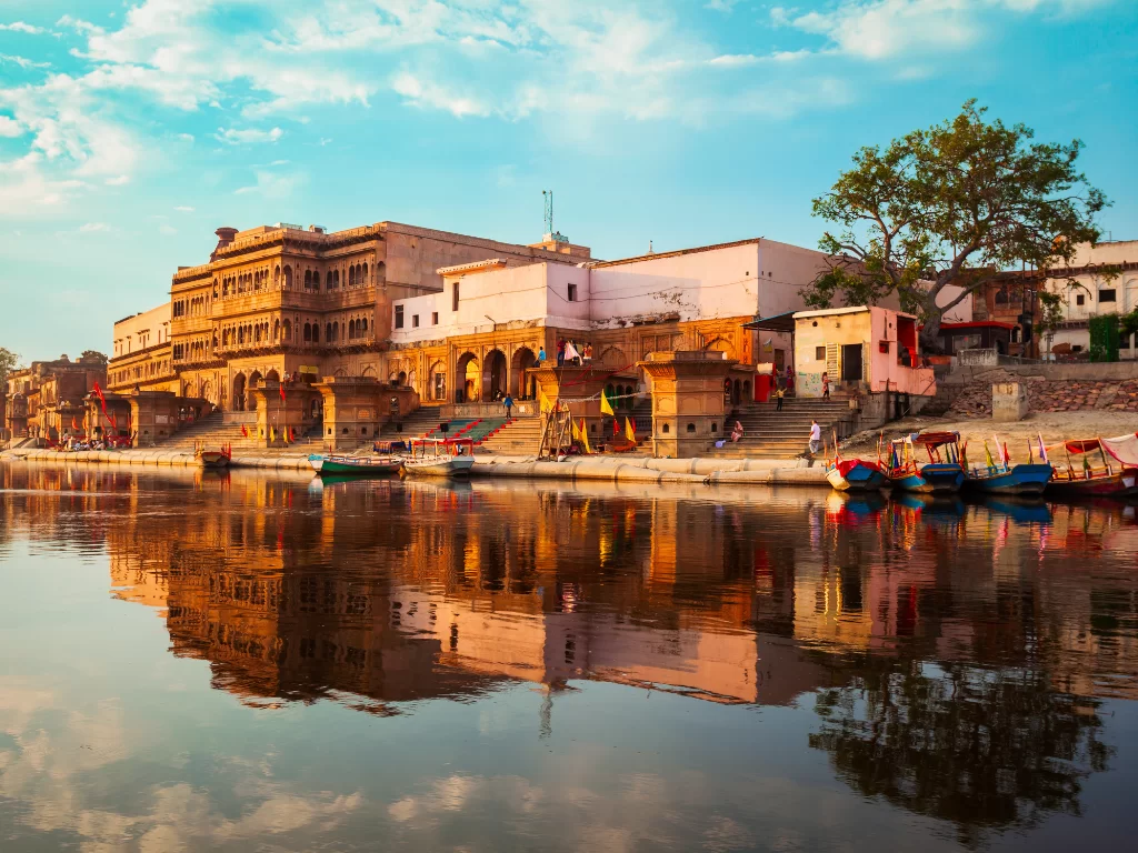 Sandstone havelis at Kusum Sarovar during golden hour, featuring arched facades, colorful boats, serene lake reflections, perfect spiritual experience with Mathura Vrindavan tour package. 