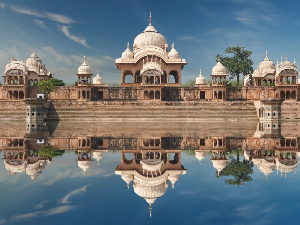 Radha Kund temples at Kusum Sarovar during clear daytime, featuring white domes, pink sandstone pavilions, serene lake reflections, perfect spiritual experience with Mathura Vrindavan tour package. 
