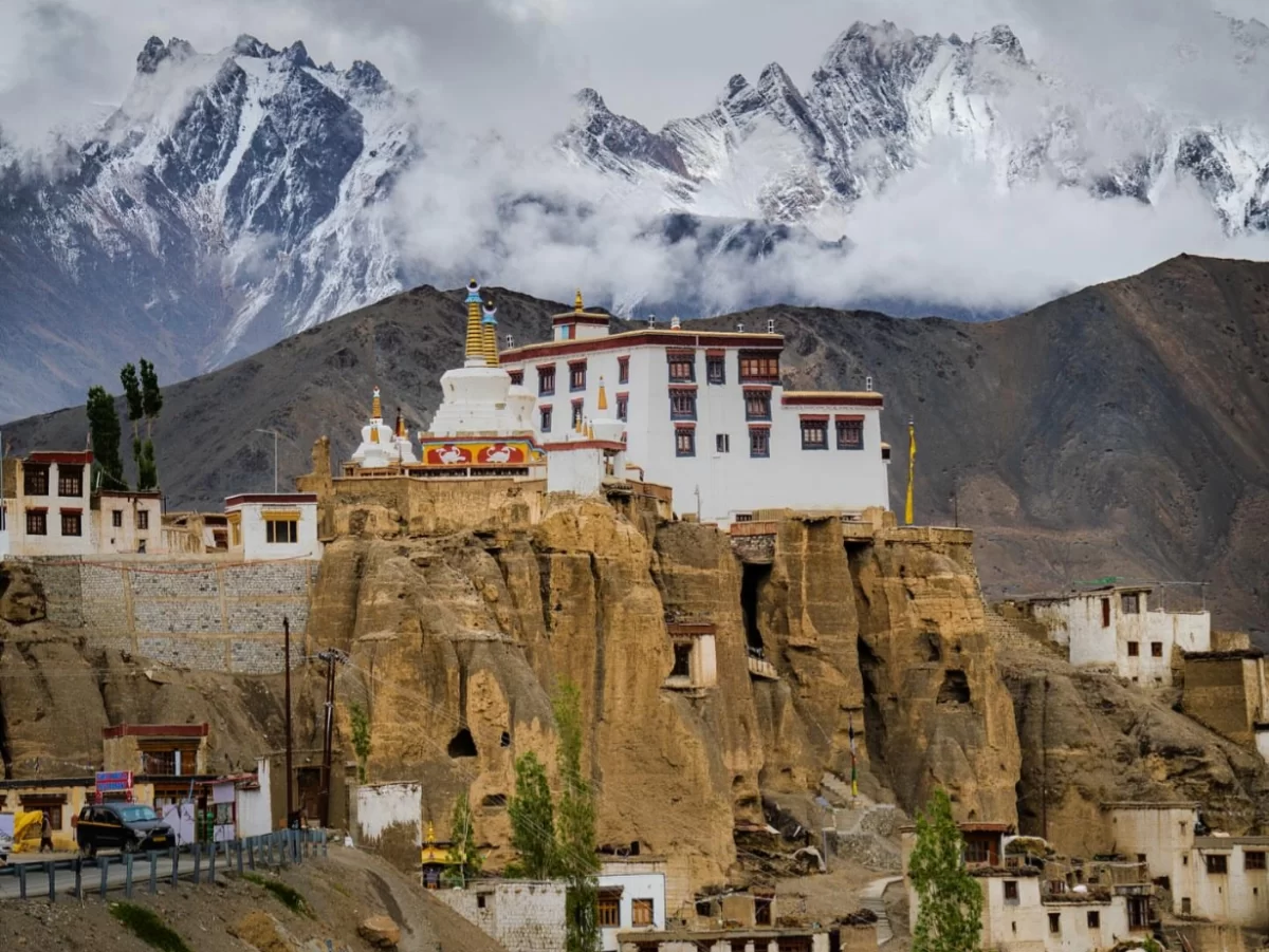Lamayuru Monastery Ladakh perched on cliffs during misty cloudy weather, featuring golden stupas and snow-capped peaks, perfect spiritual Ladakh tour package.