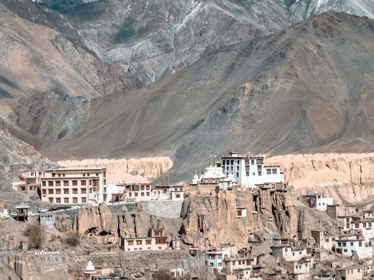 Stunning panoramic view of Lamayuru Monastery perched on dramatic eroded cliffs amid lunar moonscape landscapes, traditional white-washed Ladakhi buildings, and rugged Himalayan mountains in the background. Lamayuru tour packages.