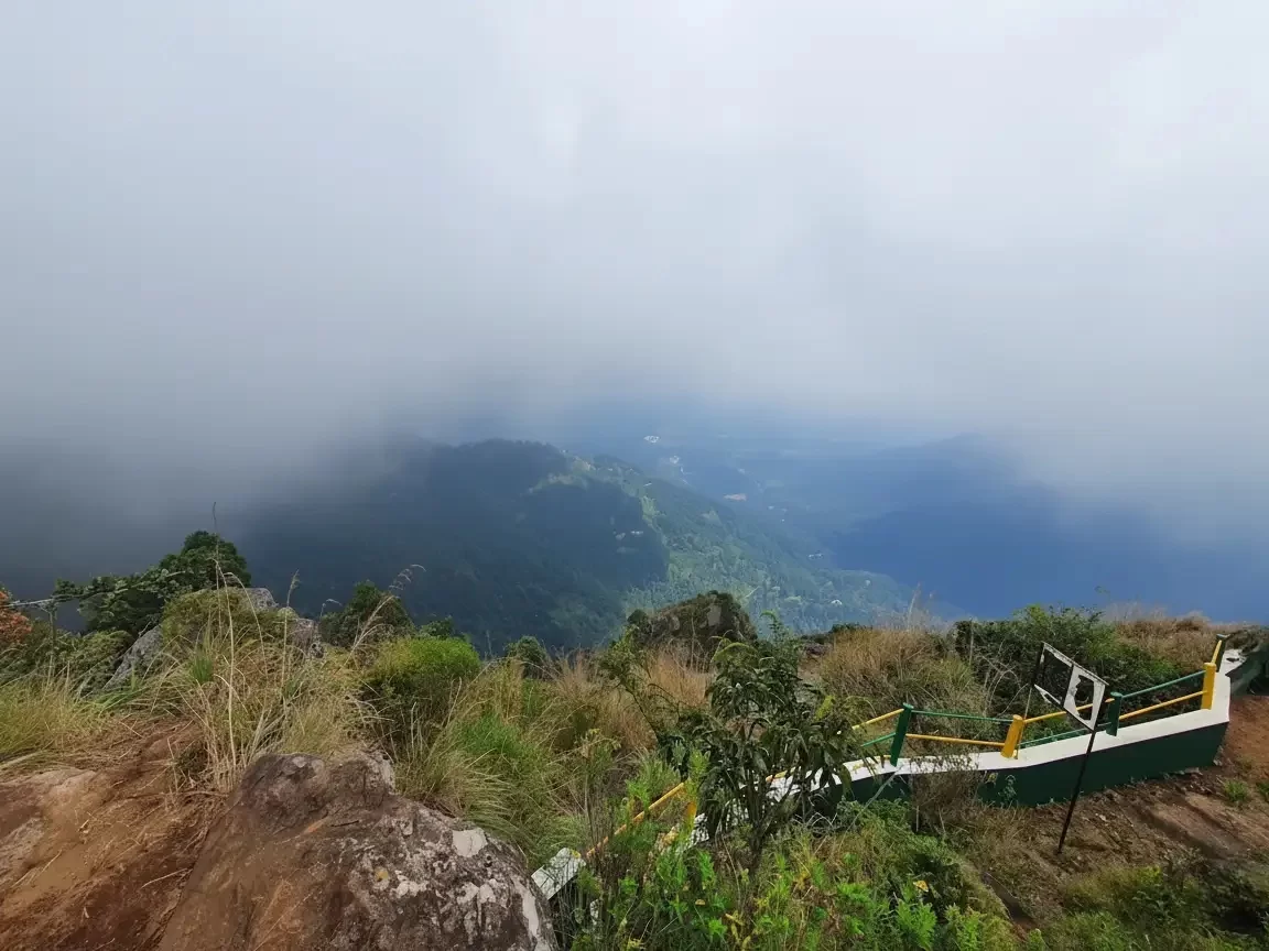 Mist-covered valley view from Lamb's Rock viewpoint in Coonoor, Nilgiri Hills, featuring rugged cliffs and greenery.