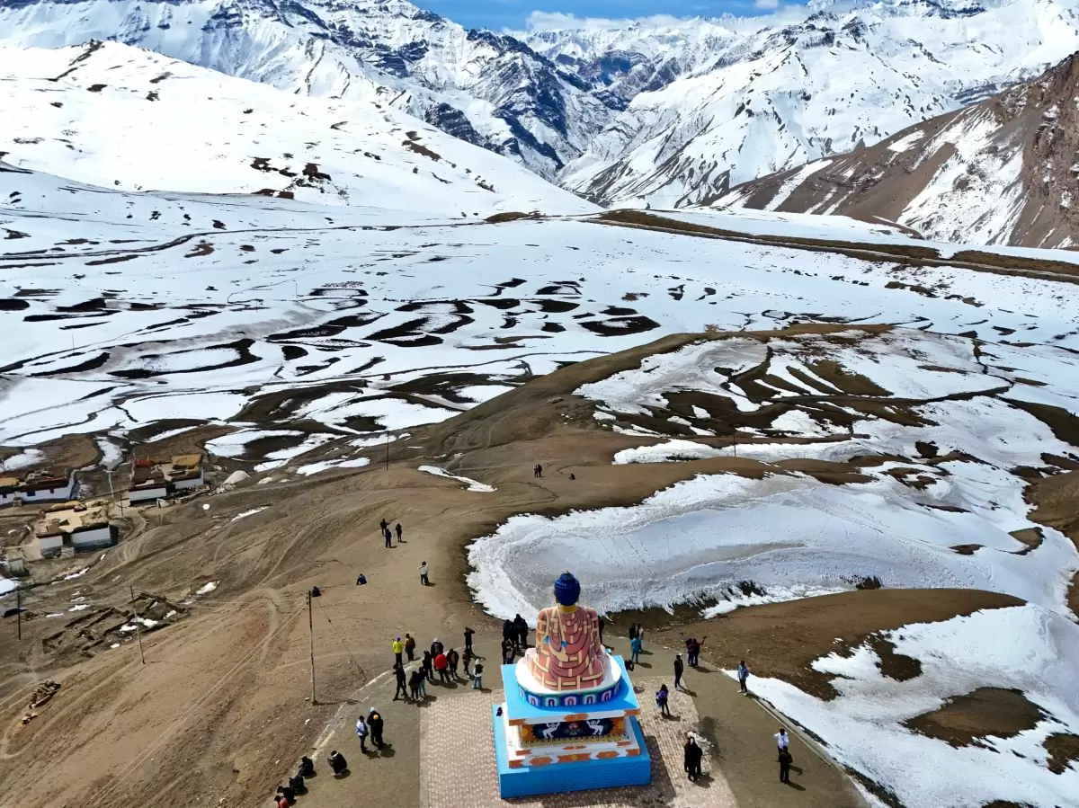 Langza Village Buddha statue near Kaza during snowy winter, featuring tourists prayer flags snow covered valleys mountains, perfect cultural experience Himachal tour package.