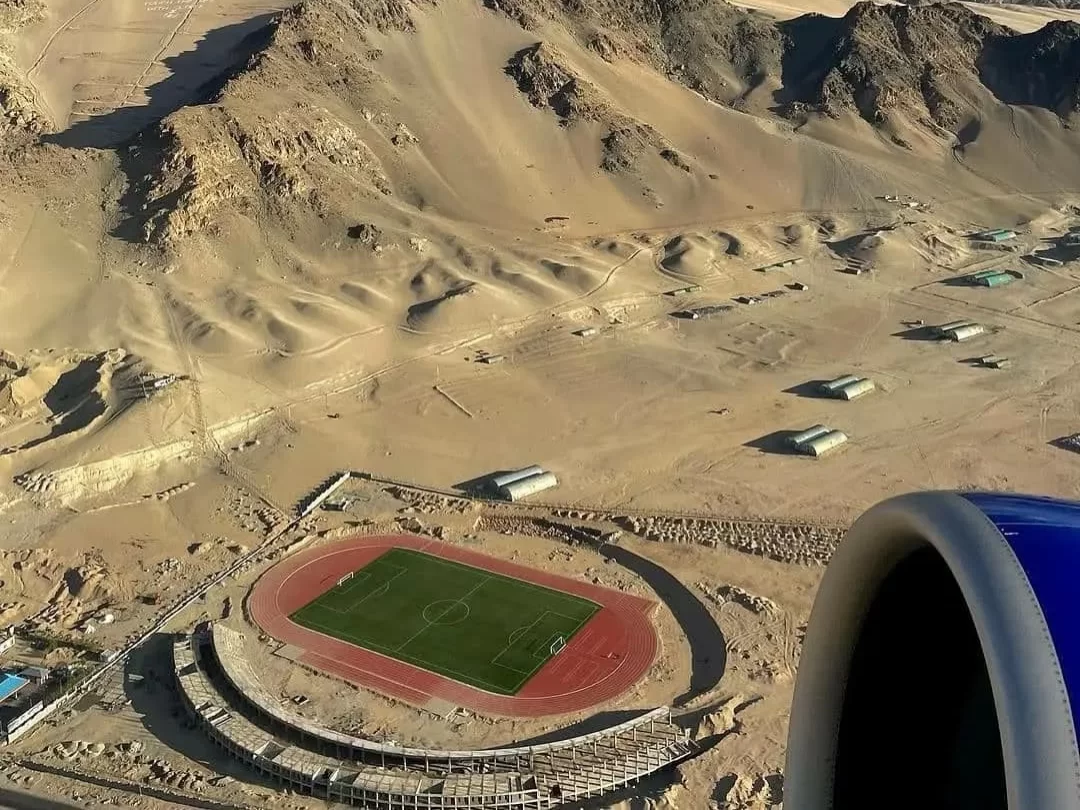 Aerial view of Leh stadium from Leh flight window during daytime, featuring desert mountains and aircraft engine, perfect Leh Ladakh tour package