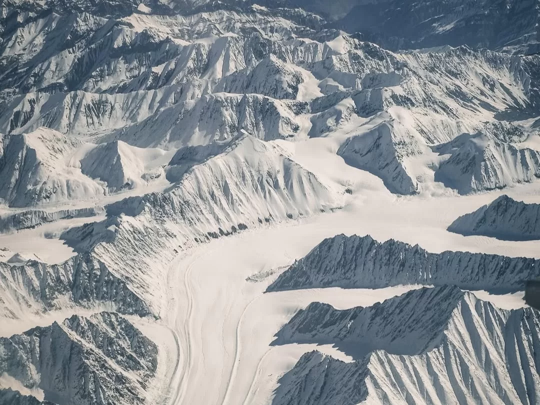 Glacier valleys and snow-clad Himalayan peaks from Leh flight window, featuring dramatic ridges and ice fields, perfect Leh Ladakh tour package