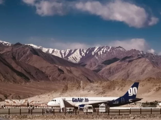 Leh airport runway with GoAir flight during daytime, featuring barren mountains and snow peaks, perfect Leh Ladakh tour package