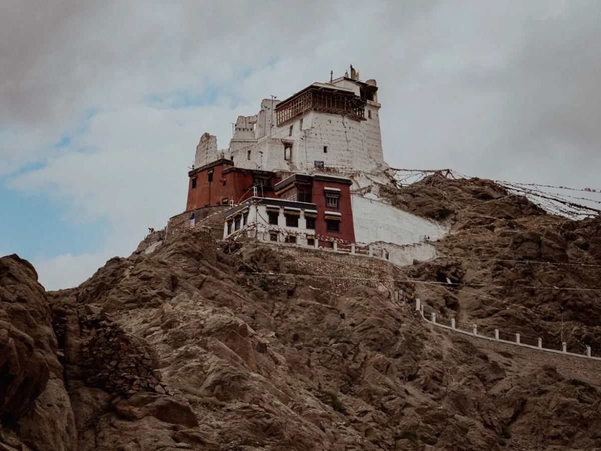 Leh Palace Ladakh majestic white nine-storey former royal palace with red tower perched on rocky hill amid prayer flags, dramatic cloudy sky, iconic Himalayan heritage adventure tour package.