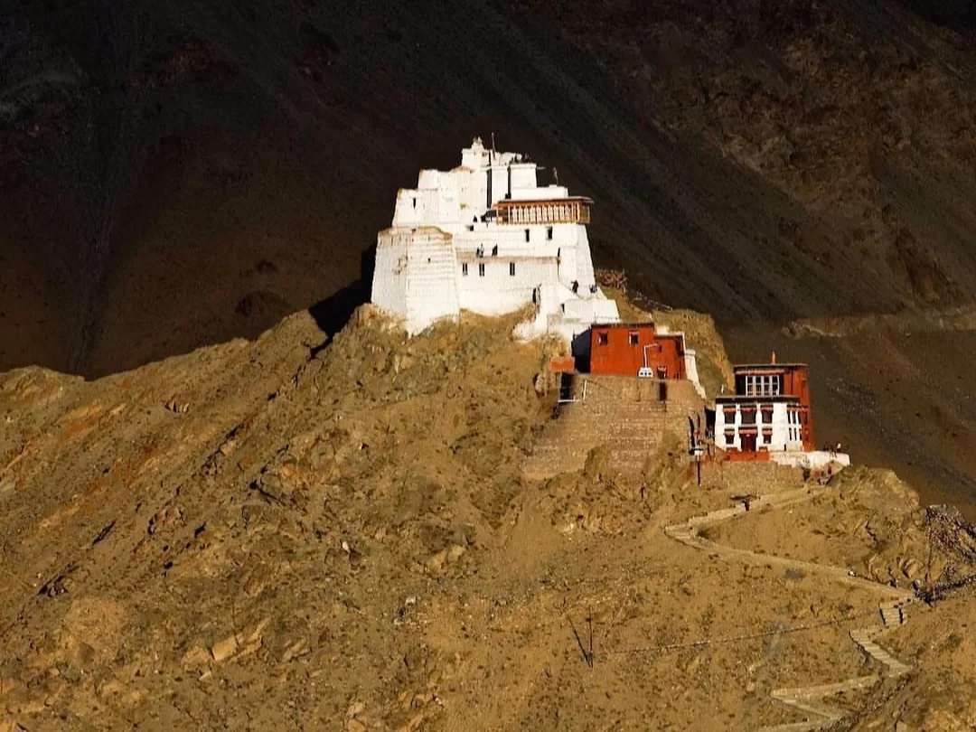 Leh Palace Ladakh twilight silhouette of towering white multi-levelled monastery with red accents on barren brown hill dramatic dark mountains backdrop, mystical Himalayan spiritual tour package.