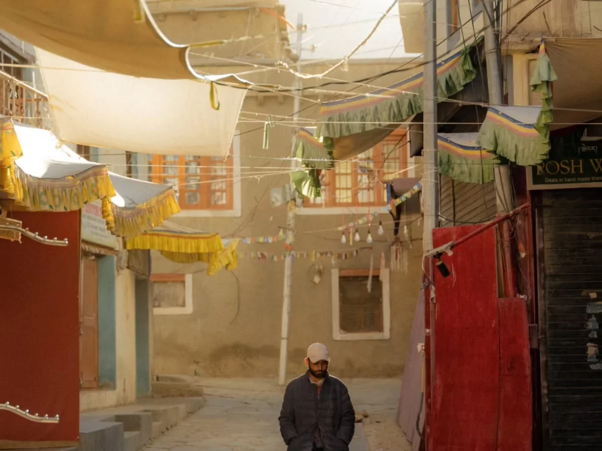 Leh old town street near Leh Palace with colorful prayer flags, yellow green awnings, traditional Ladakhi houses, lone man walking under prayer flags, perfect India tour package.