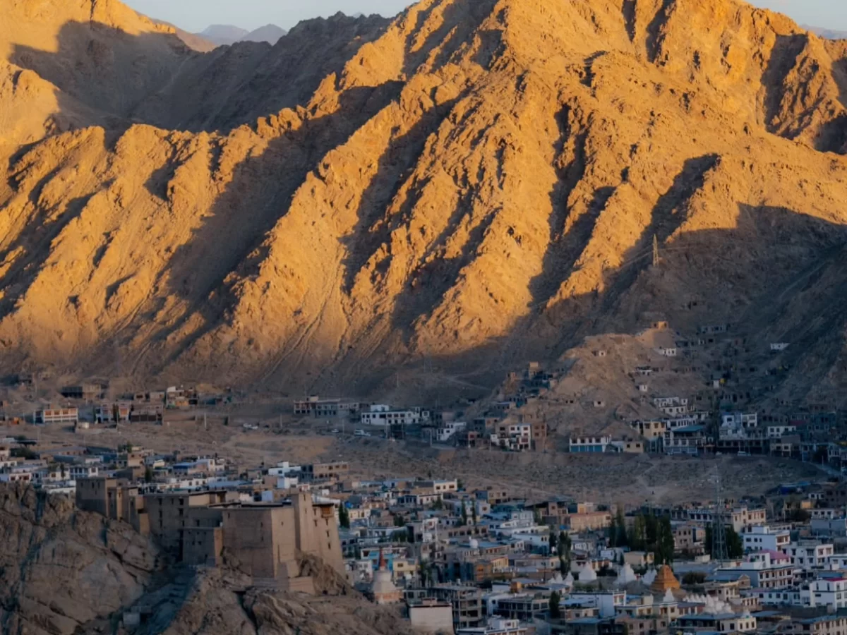 Leh Palace overlooking Leh town with traditional white mud-brick buildings nestled against dramatic golden-hour rugged Himalayas mountains, perfect India tour package.