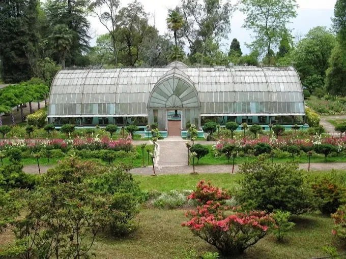 Lloyd Botanical Garden in Darjeeling, West Bengal, featuring a glass conservatory surrounded by landscaped flower beds and tall Himalayan trees, a well-known attraction included in West Bengal tour packages.