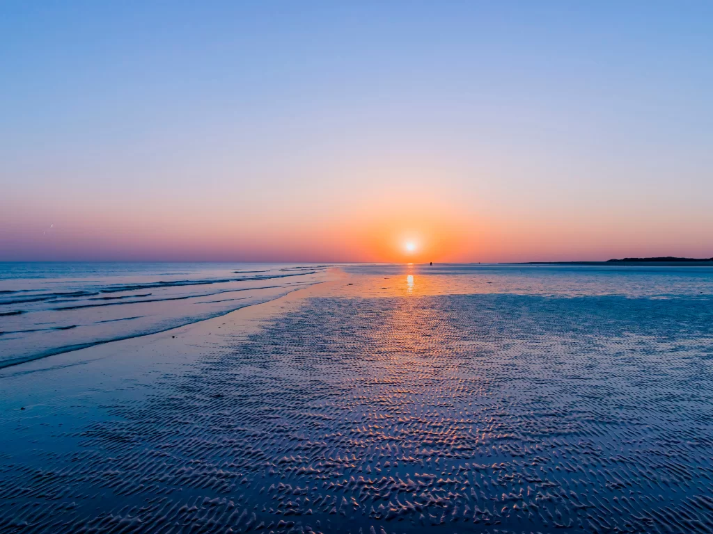 Mandvi Beach sunset at Kutch Gujarat during golden hour, featuring orange-pink skies, glowing sun reflections on white sands and Arabian Sea waves, perfect romantic experience with Gujarat tour packages.