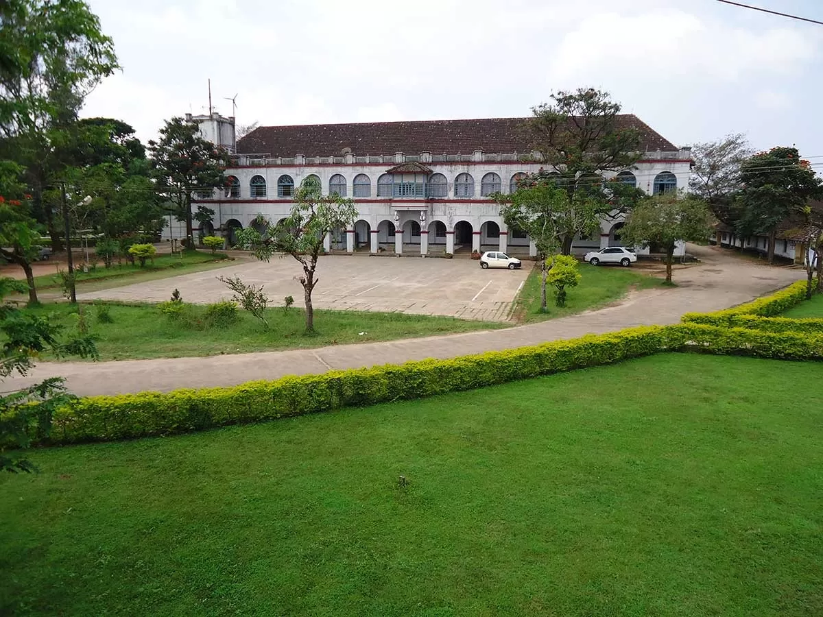 Madikeri Fort at Madikeri Coorg during cloudy day, featuring white colonial building, arches, courtyard, trees, vehicles, perfect cultural experience Karnataka tour packages.