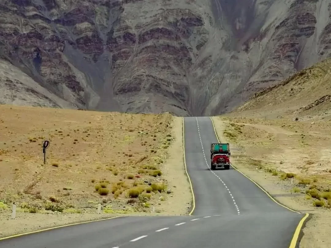 Magnetic Hill Ladakh Leh-Kargil highway optical illusion gravity hill red Maruti Gypsy jeep parked uphill appearing rolling forward barren desert valley dramatic barren Zanskar mountains foggy horizon, mysterious tourist attraction adventure tour package.