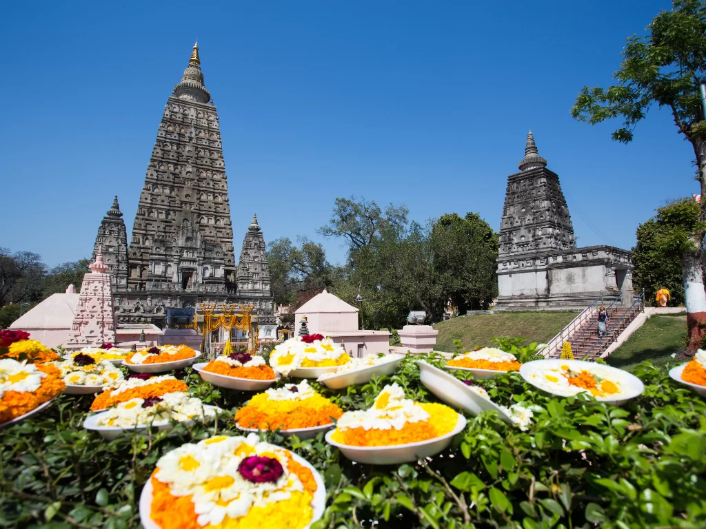 Mahabodhi Temple stupas with flower offerings in Bodh Gaya during sunny day, featuring ancient towers garlands trees lawns, perfect Bihar tour package.