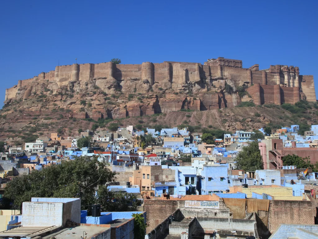 Mehrangarh Fort cityscape during sunny day, featuring massive pink ramparts atop hill overlooking blue buildings of Jodhpur, perfect cultural heritage Rajasthan tour packages. 