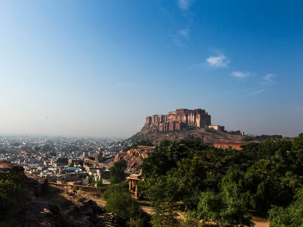 Mehrangarh Fort panoramic view during golden hour, featuring majestic pink ramparts atop rocky hill overlooking Jodhpur city, blue sky, perfect cultural heritage Rajasthan tour packages. 