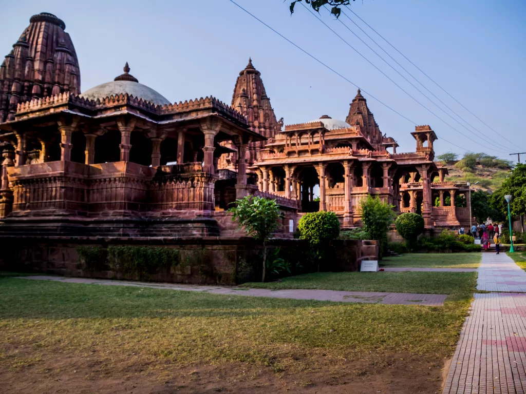 Mandore Garden temples at Jodhpur during sunny day, featuring red sandstone shikharas, domes, pavilions, lawns, perfect heritage experience Rajasthan tour packages.