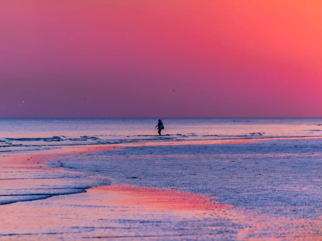Mandvi Beach sunset at Kutch Gujarat during golden hour, featuring silhouetted person, crimson skies, glowing sun reflections on white sands and Arabian Sea waves, perfect romantic experience with Gujarat tour packages.