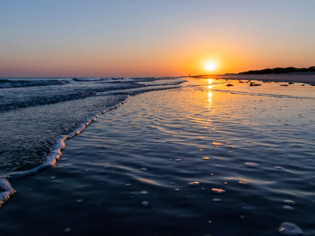 Mandvi Beach sunset at Kutch Gujarat during golden hour, featuring glowing sun, blue-orange skies, golden waves and sandy shoreline, perfect romantic experience with Gujarat tour packages.