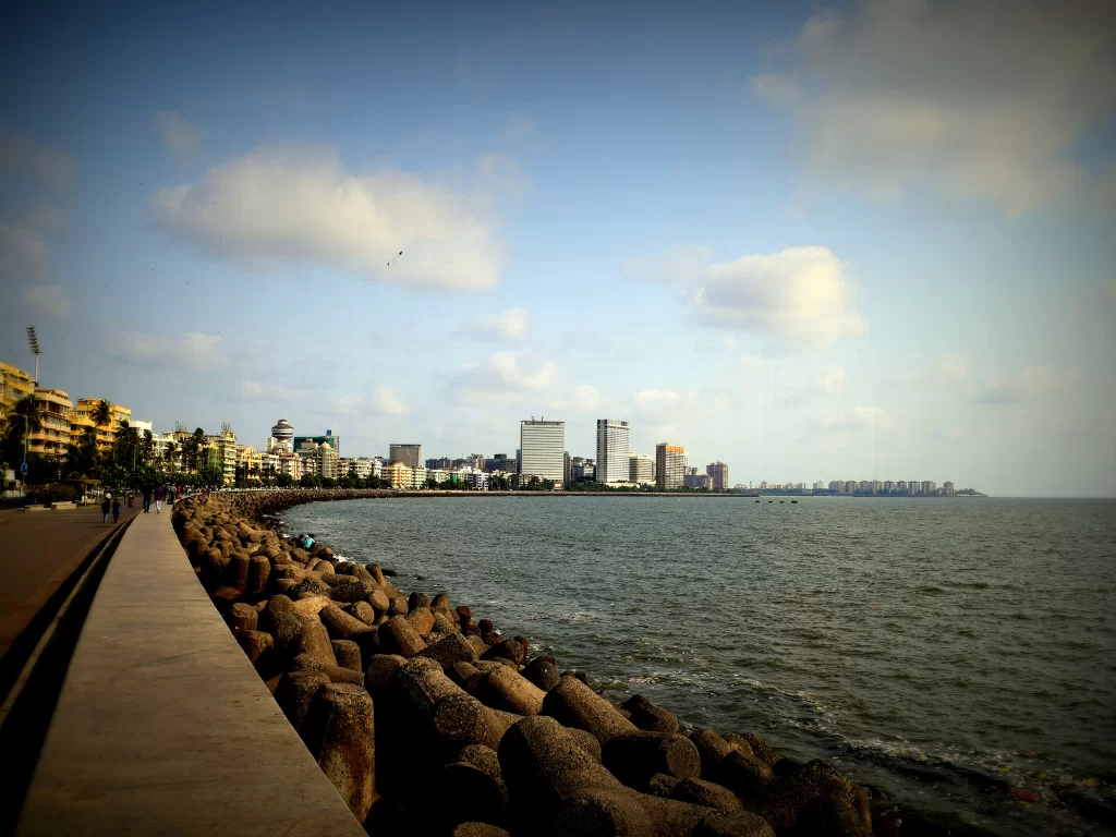 Marine Drive Mumbai promenade walkway tetrapods foreground walkers skyline cloudy blue sky Arabian Sea, perfect South Mumbai walking tour sunset photography package. 