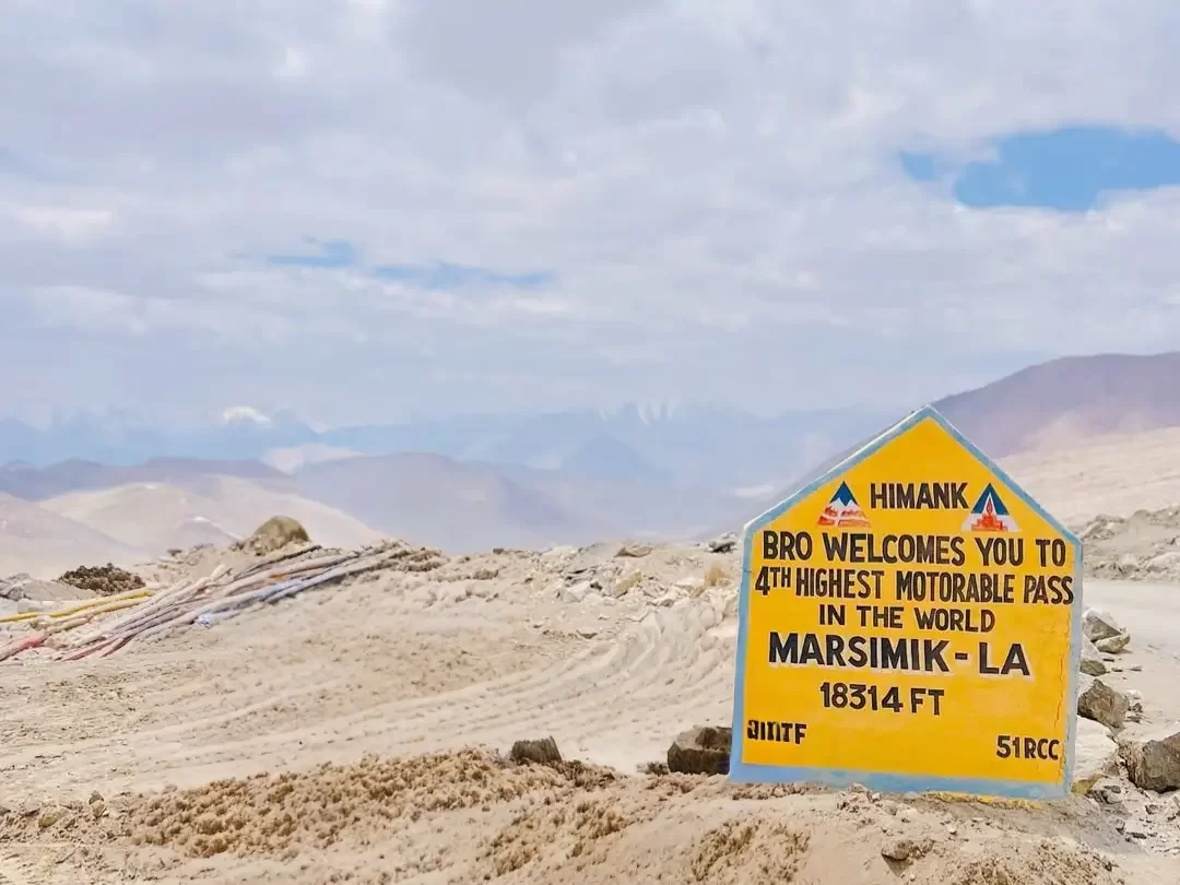 Marsimik La signboard Ladakh during clear partly cloudy day, featuring Himank BRO plaque 4th highest motorable pass 18314 ft, desert mountains, perfect adventure Ladakh tour package.