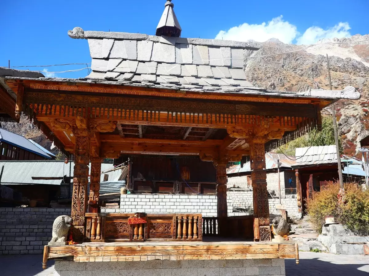 Mathi Temple Chitkul Kinnaur Himachal Pradesh during clear blue skies, featuring intricately carved wooden temple pavilion stone roof snowy mountains backdrop, perfect cultural experience Himachal tour package.