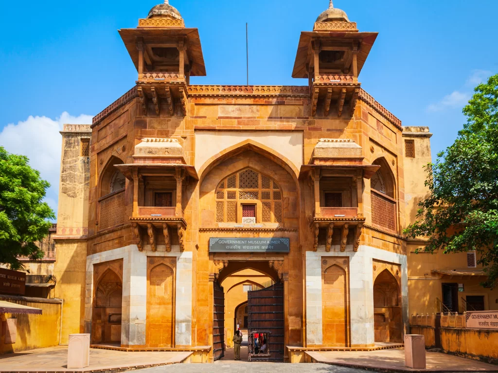 Government Museum Ajmer Rajasthan frontal Akbari Fort main gate sandstone Mughal Rajput architecture chhatris jharokhas arched entranceway trees rickshaw blue sky historical artifacts museum entry.