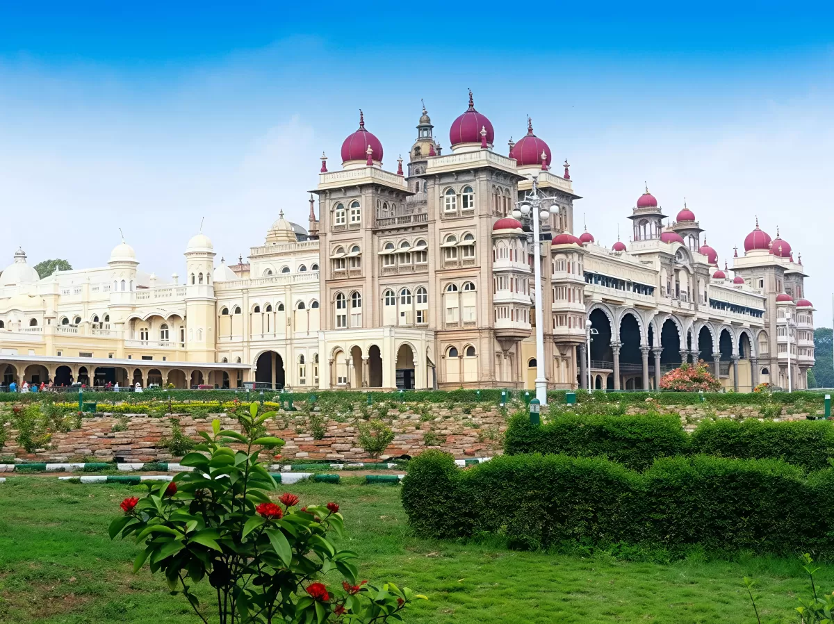 Mysore Palace grand facade at Mysuru Karnataka during sunny day, featuring Indo-Saracenic domes red towers gardens lawns, perfect royal heritage Karnataka tour package.