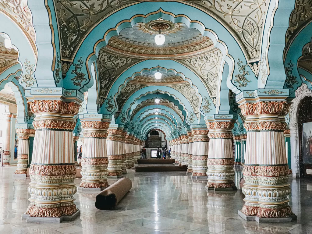 Ornate Durbar Hall of Mysore Palace during daytime, featuring turquoise arches, carved pillars and reflective marble floor, perfect royal Karnataka tour package