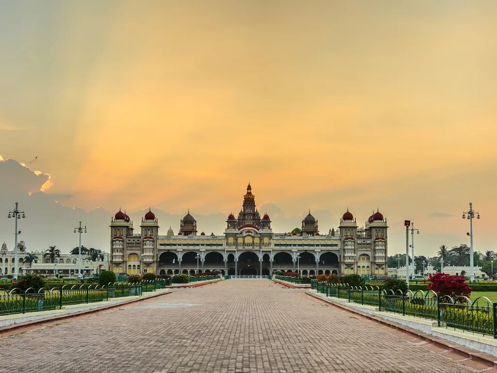 Mysore Palace at sunset, featuring glowing sky, grand arches and manicured gardens along central walkway, perfect royal Karnataka tour package