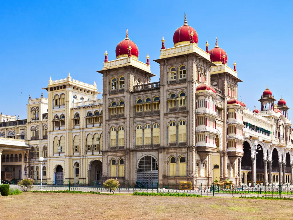Mysore Palace side view during clear daytime, featuring red domes, arched windows and open courtyard, perfect royal Karnataka tour package