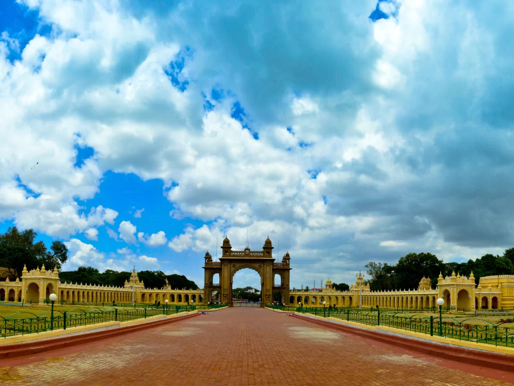 Mysore Palace gateway in daytime, featuring dramatic clouds, central arch and red-brick pathway, perfect royal Karnataka tour package