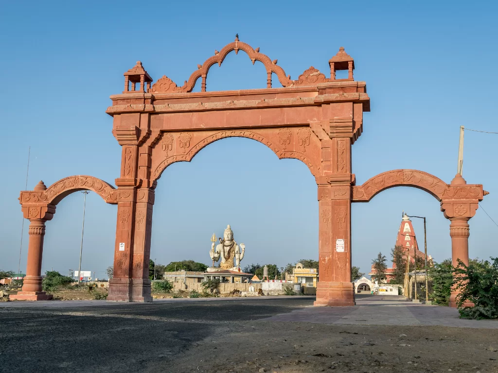 Nageshwar Jyotirlinga Temple entrance in Dwarka during clear day, featuring red sandstone toran gate with Shiva statue and temple spire visible, perfect pilgrimage experience with Gujarat tour packages.