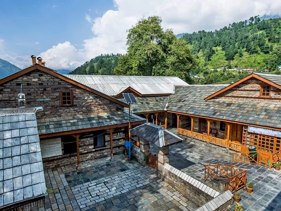 Naggar Castle in Kullu featuring traditional stone and wood architecture with slate roofs, courtyard, and scenic Himalayan hills in the background.
