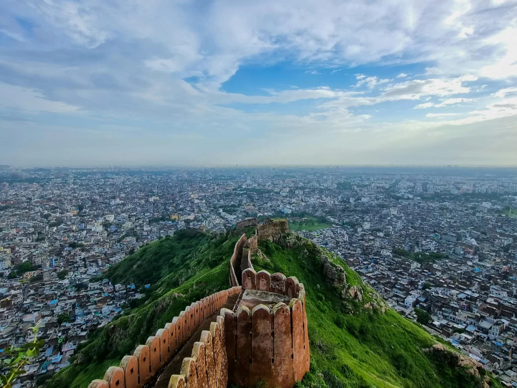 Jaipur city panoramic view from Nahargarh Sunset Point during golden hour, featuring ancient walls Aravalli hills, perfect romantic experience Rajasthan tour packages.