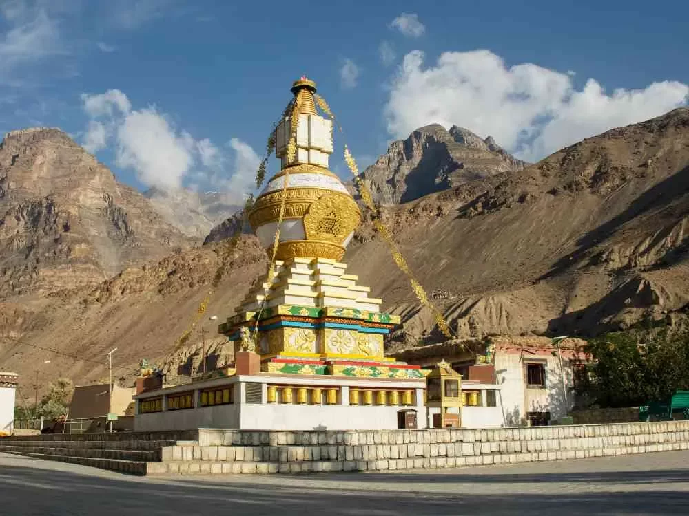 Nako Monastery Spiti Valley during partly cloudy skies, featuring golden stupa colorful prayer flags white buildings barren mountains, perfect spiritual experience Himachal Pradesh tour package.