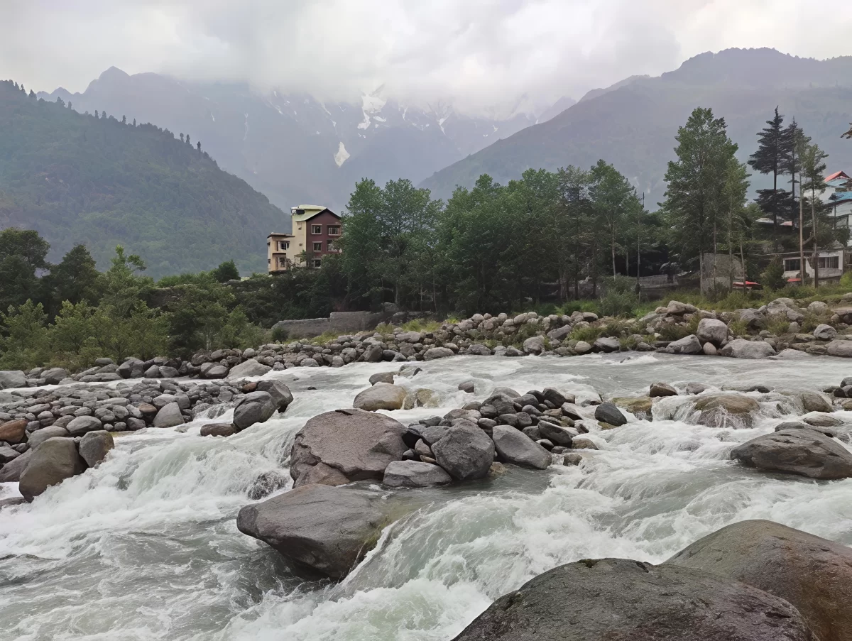 Rushing river at Nehru Kund Manali during misty weather, featuring rocky banks pine forests and snow peaks, perfect nature experience Himachal Pradesh tour package.
