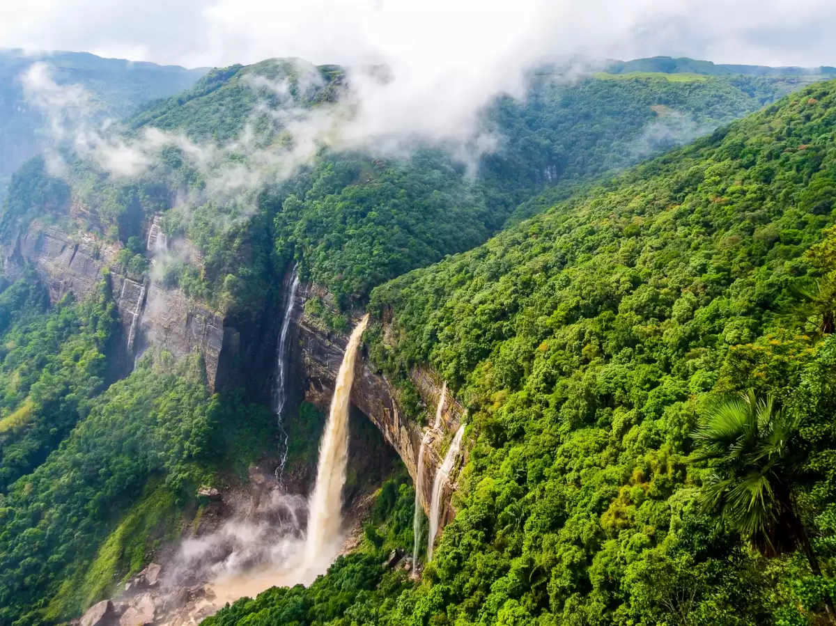 Nohkalikai Falls Cherrapunji during cloudy day, featuring aerial view multiple waterfalls misty green forested valleys mountains, perfect nature adventure Cherrapunji Meghalaya tour package.