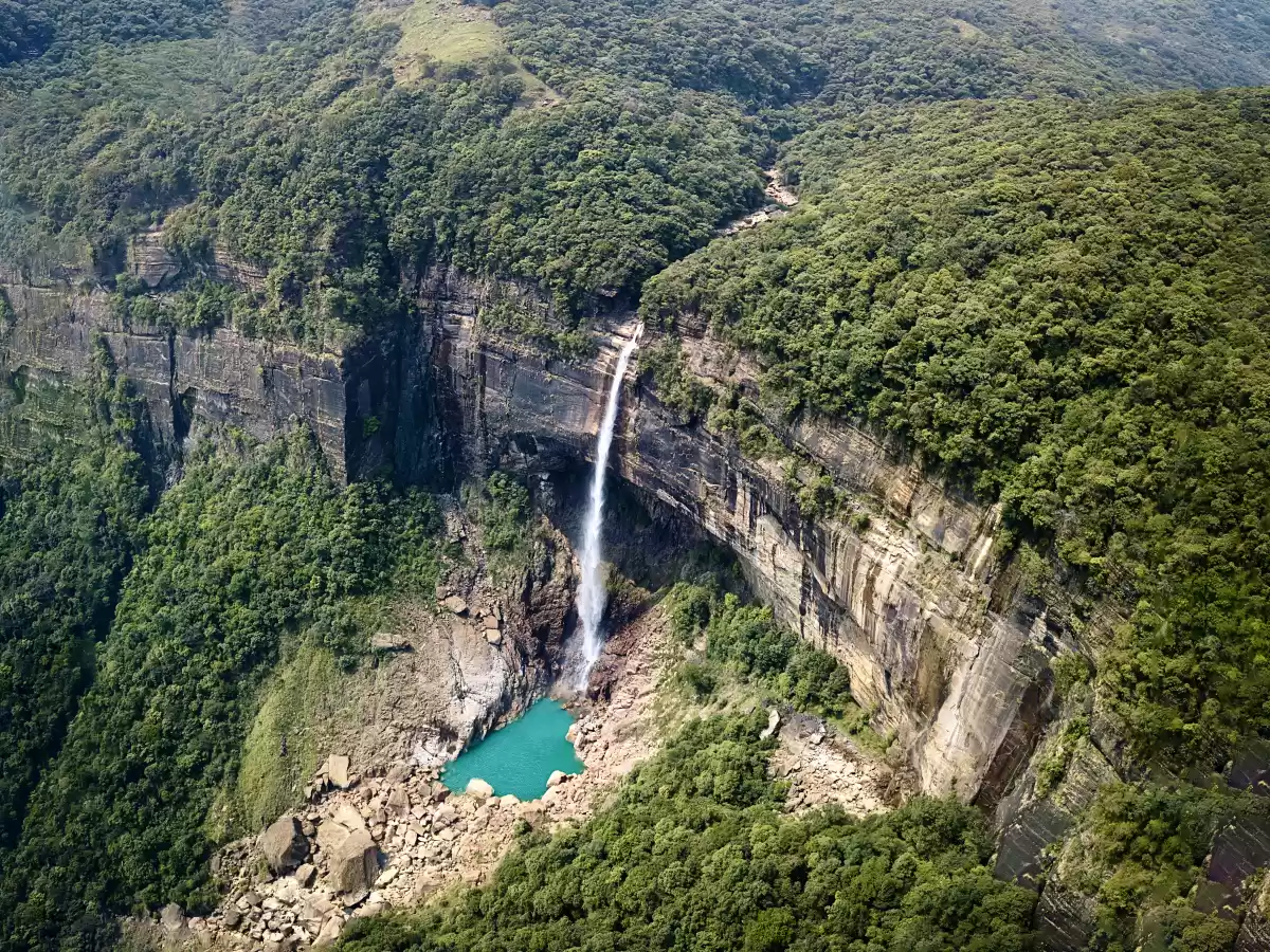 Nohkalikai Falls Cherrapunji during sunny day, featuring aerial view tallest plunge waterfall turquoise pool lush green forested cliffs valley, perfect nature adventure Cherrapunji Meghalaya tour package.