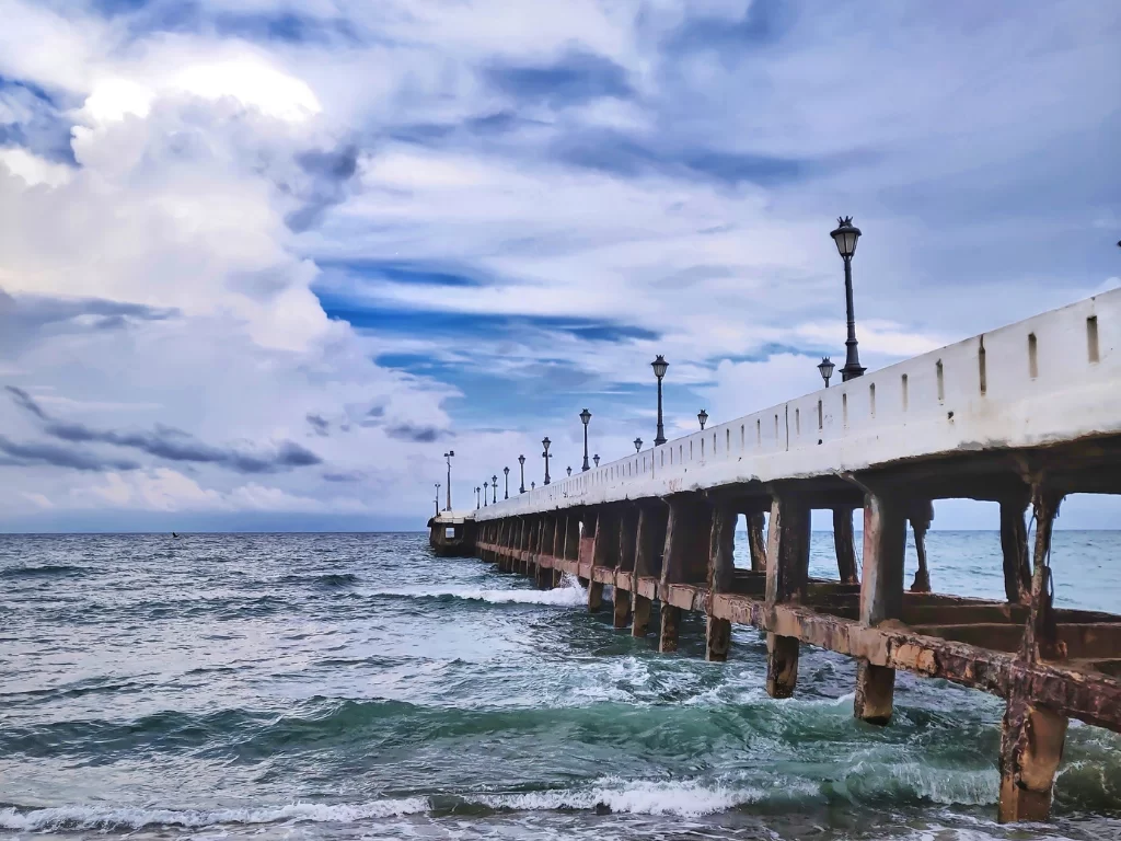 Old pier at Promenade Beach Puducherry during cloudy skies, featuring lamp posts and ocean waves, perfect romantic experience Puducherry tour package.