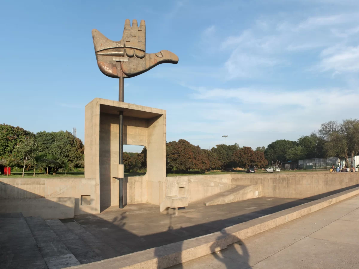 Iconic Open Hand Monument at Chandigarh during clear sky, featuring hand bird sculpture, concrete pedestal, trees, perfect cultural Chandigarh tour package.