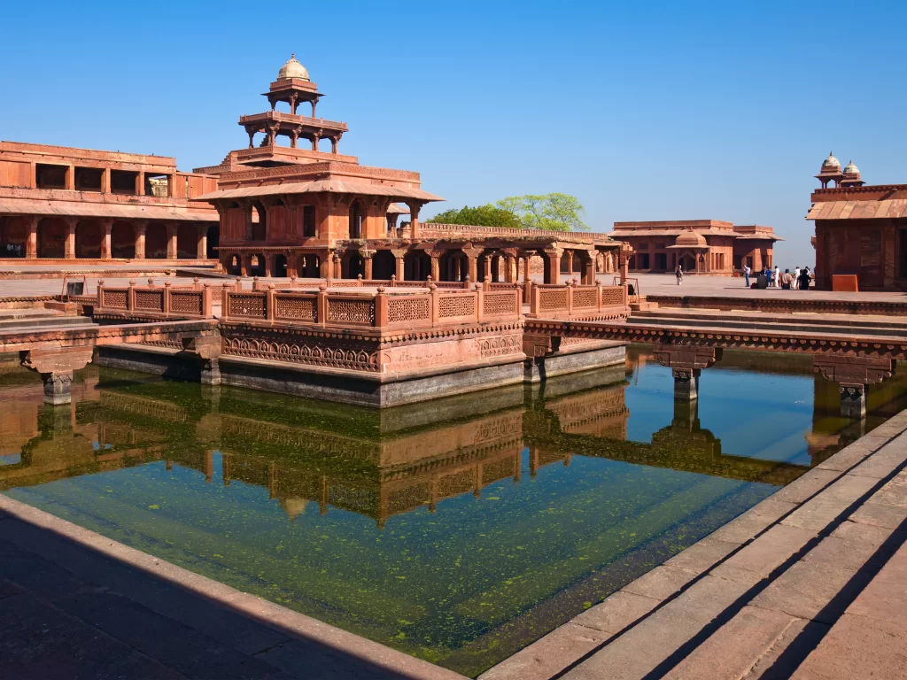 Panch Mahal at Fatehpur Sikri Uttar Pradesh during clear skies, featuring red sandstone pavilions, domes, arches, reflections in Anup Talab, perfect heritage experience Agra tour package.