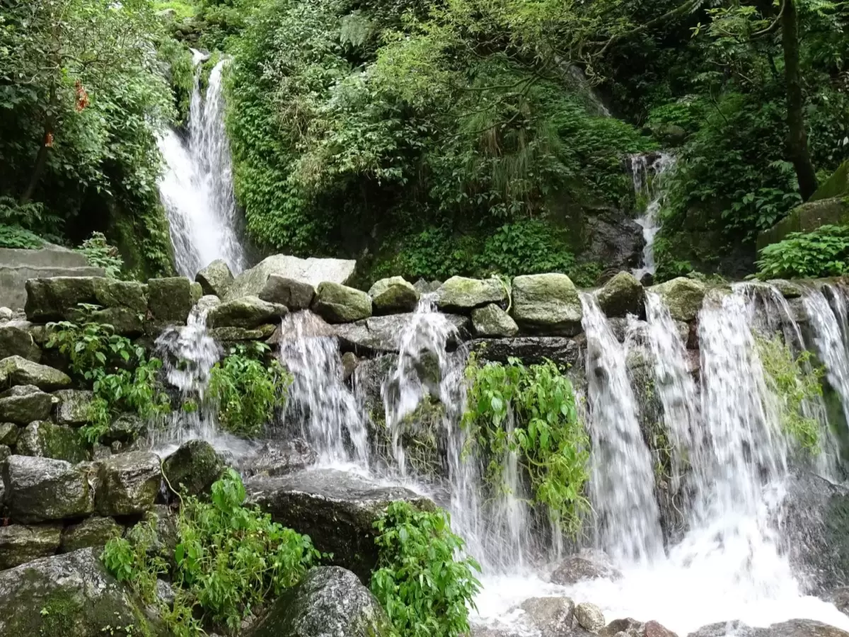 Cascading Panchpula waterfall at Dalhousie during misty monsoon, featuring lush green forests, rocky cascade, perfect adventure Himachal Pradesh tour package.
