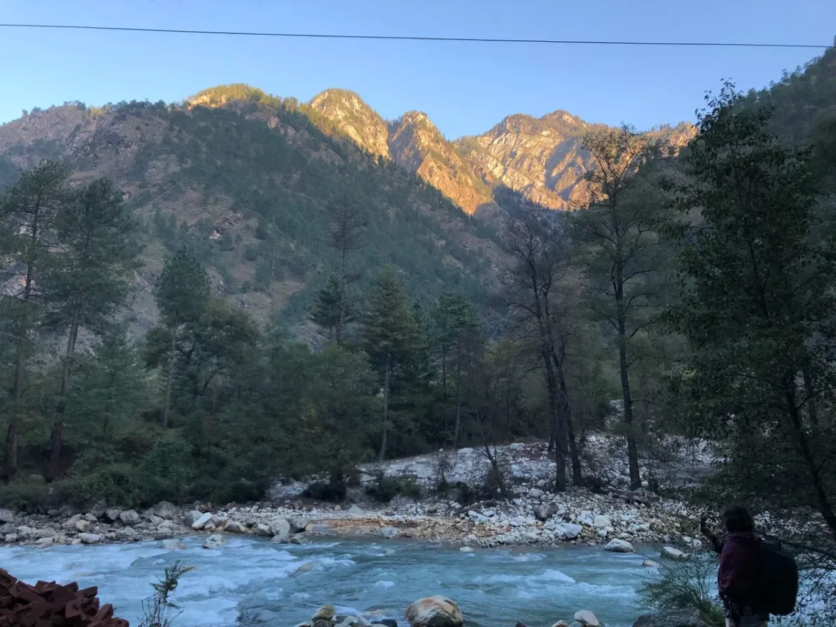 Parvati River Kasol Parvati Valley Himachal Pradesh during golden hour sunset lighting, featuring turquoise rapids rocky banks pine forested rugged Himalayan peaks backpacker foreground, perfect cultural experience Himachal tour package.