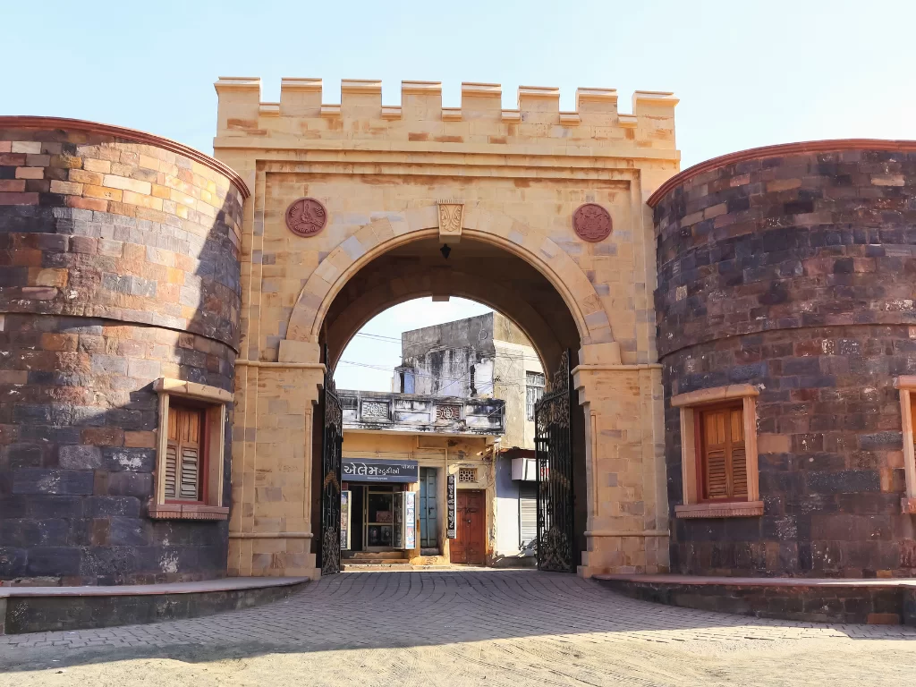 Prag Mahal entrance gate in Bhuj, Kutch during clear day, featuring Italian Gothic arched doorway, stone bastions, wooden shutters and traditional Kutchi architecture, perfect heritage landmark with Gujarat tour packages.