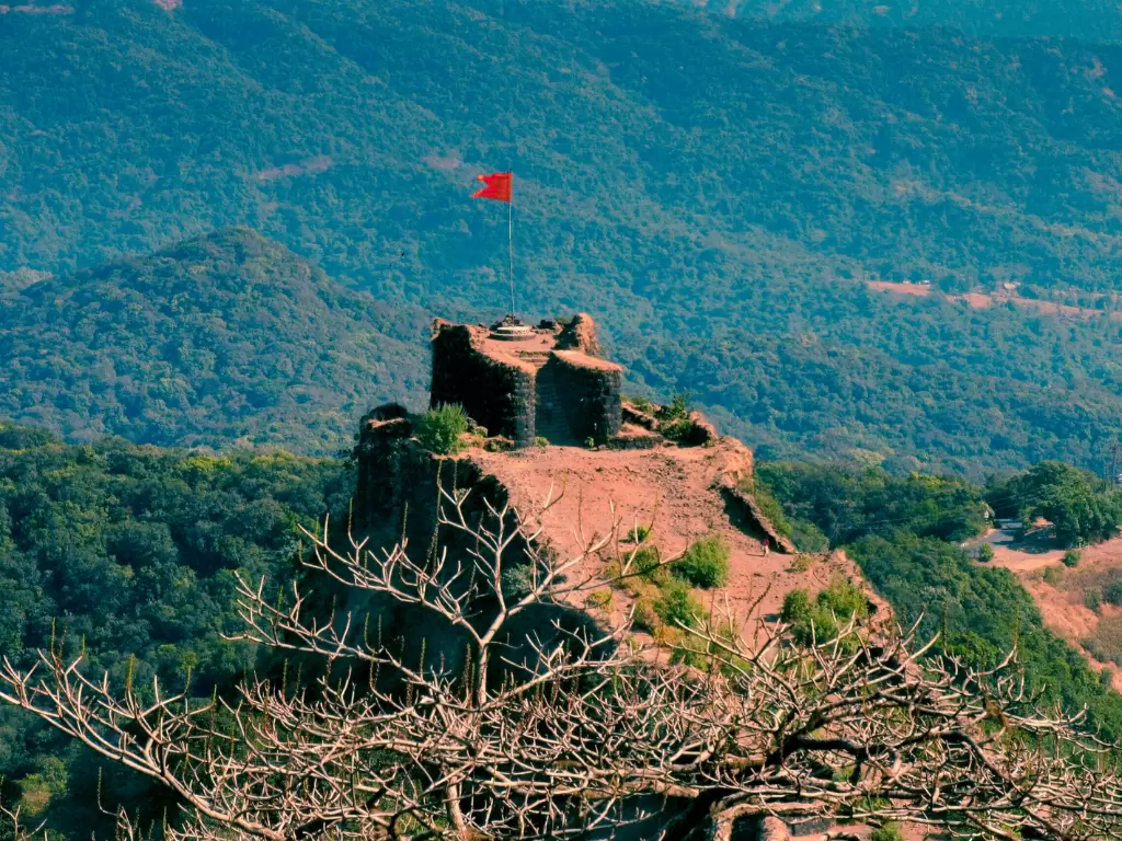 Pratapgad Fort Mahabaleshwar panoramic view, featuring ruined ramparts red saffron flag atop rocky peak surrounded lush misty Sahyadri mountains, perfect Maharashtra tour packages.