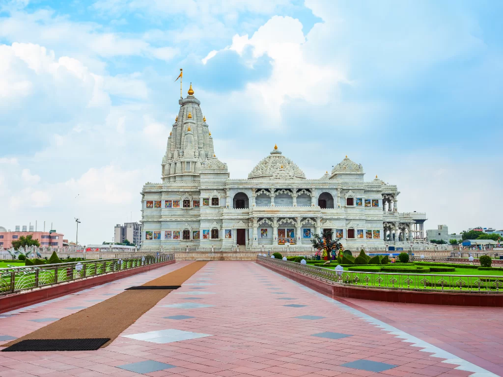 Prem Mandir at Vrindavan during partly cloudy daytime, featuring white marble facade, golden shikharas, terracotta pathways, perfect spiritual experience with Mathura Vrindavan tour package.